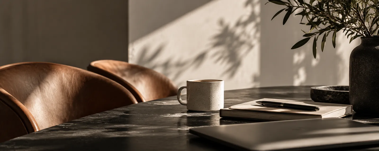 Leather chairs, coffee and notebook on a dark stone table in warm afternoon light