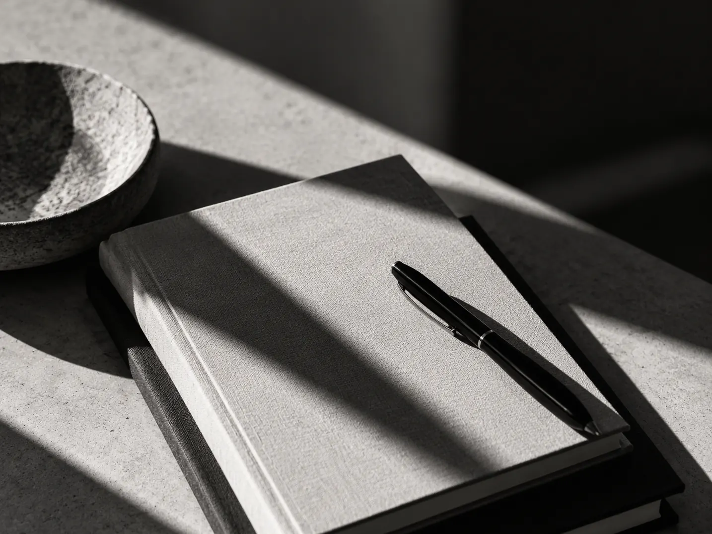Notebook and pen on a stone table in dramatic black-and-white light