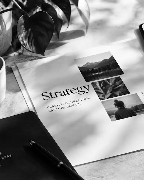 Black-and-white brand strategy flat lay — printed strategy sheet, photographs, notebook and coffee on a sunlit desk